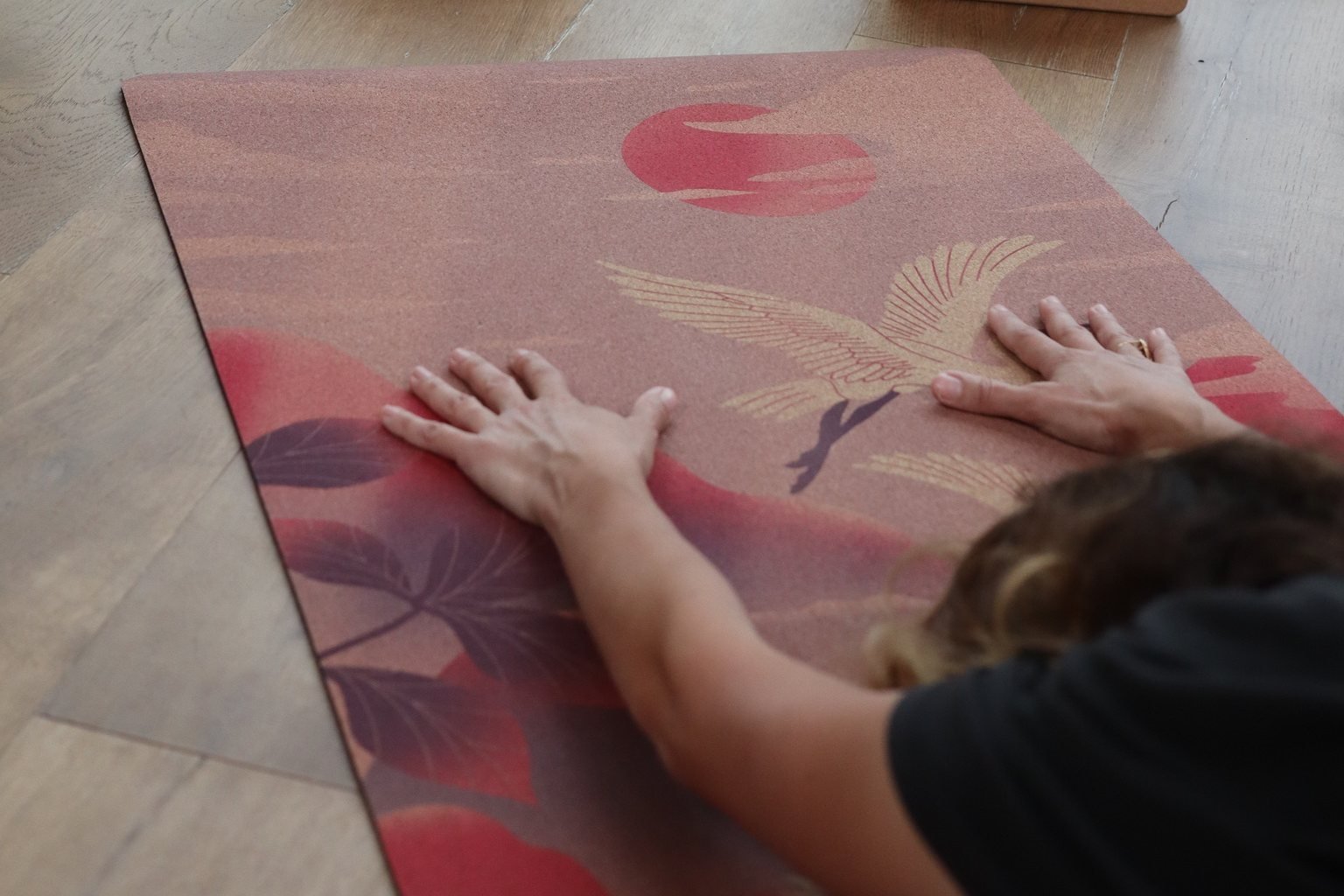 Mains posées à plat, doigts écartés, sur un tapis de yoga en liège illustré d'une grue
