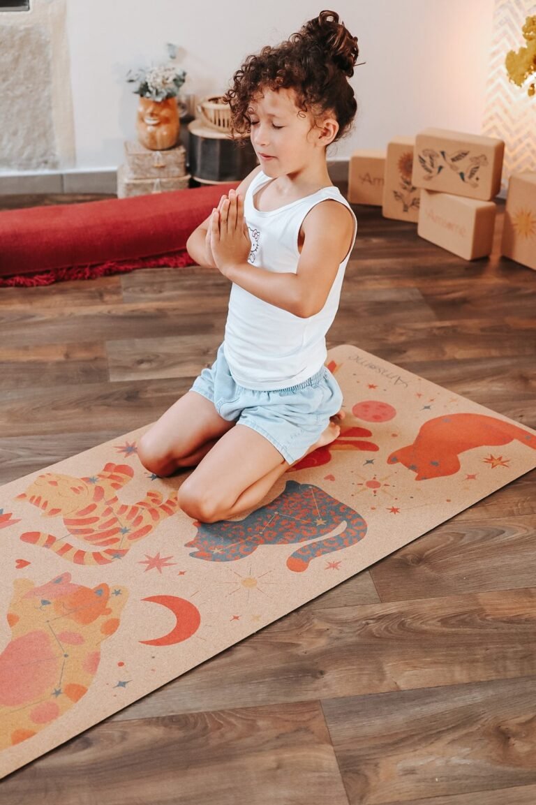 Enfant à genoux sur un tapis de yoga en liège Chats galactiques, les yeux fermés et les mains jointes