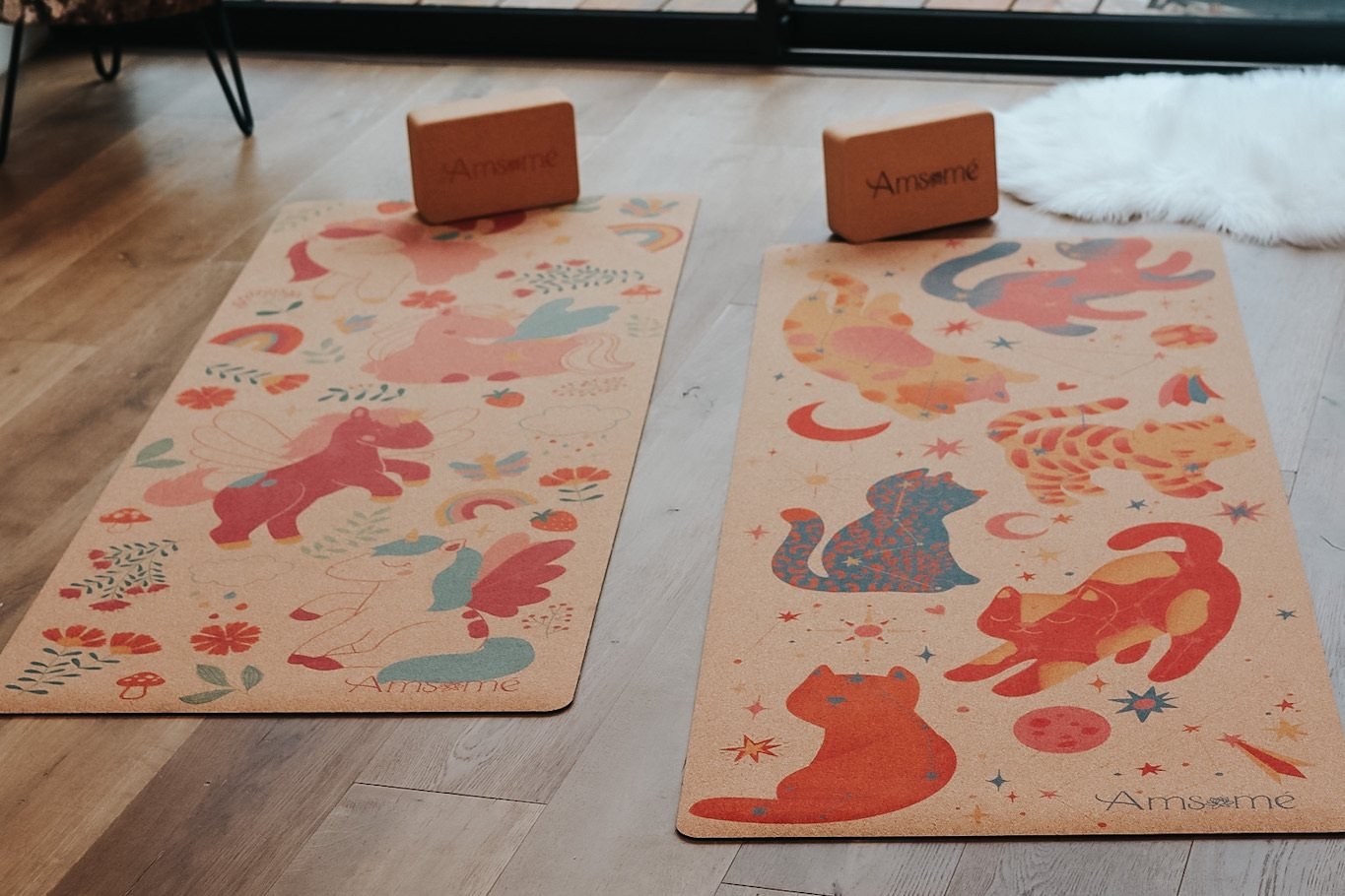 Deux tapis de yoga enfant en liège, Féérie des licornes et Chats galactiques, posés côte à côte avec deux briques sur un parquet